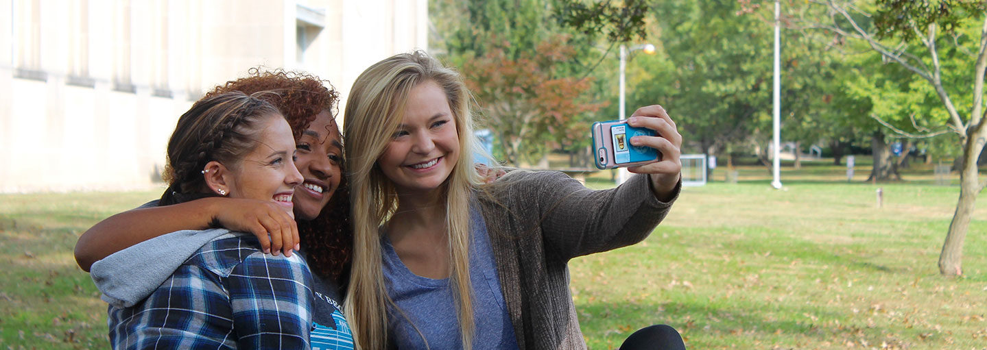Students sitting on the lawn, taking a selfie