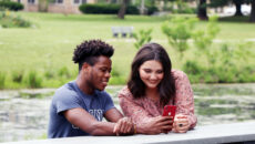 Students on a bench at the lake looking at a phone