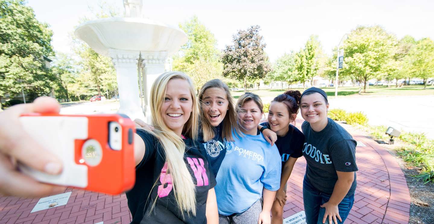 Five young women taking a selfie by fountain.