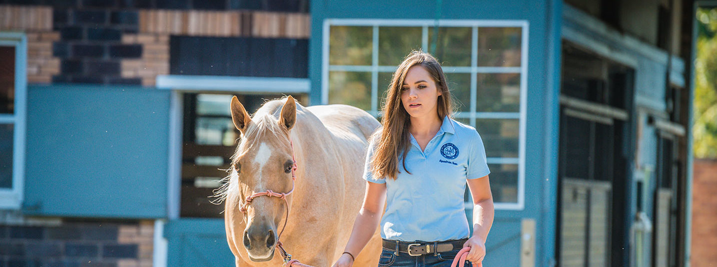 Student walking with horse outside of the barn