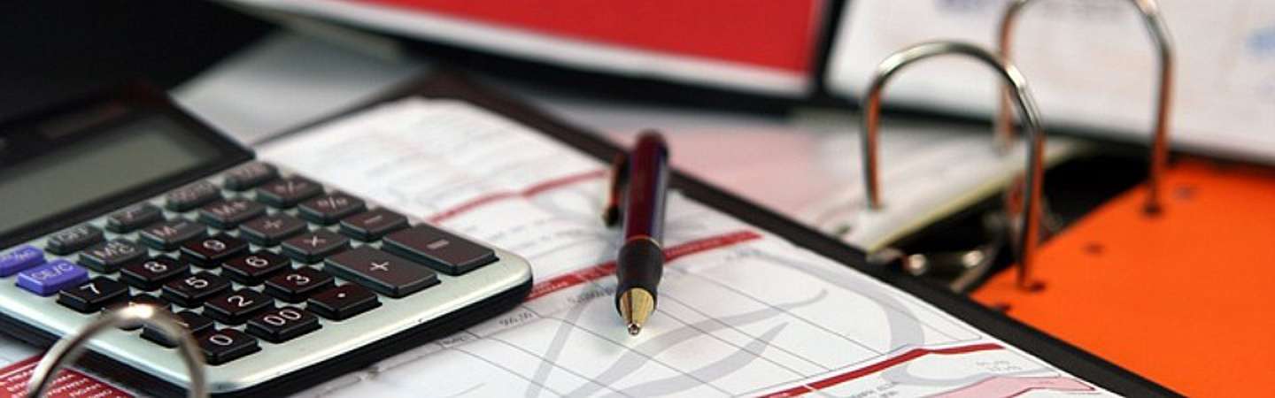 A photo of a calculator, binder, pen and accounting sheet.