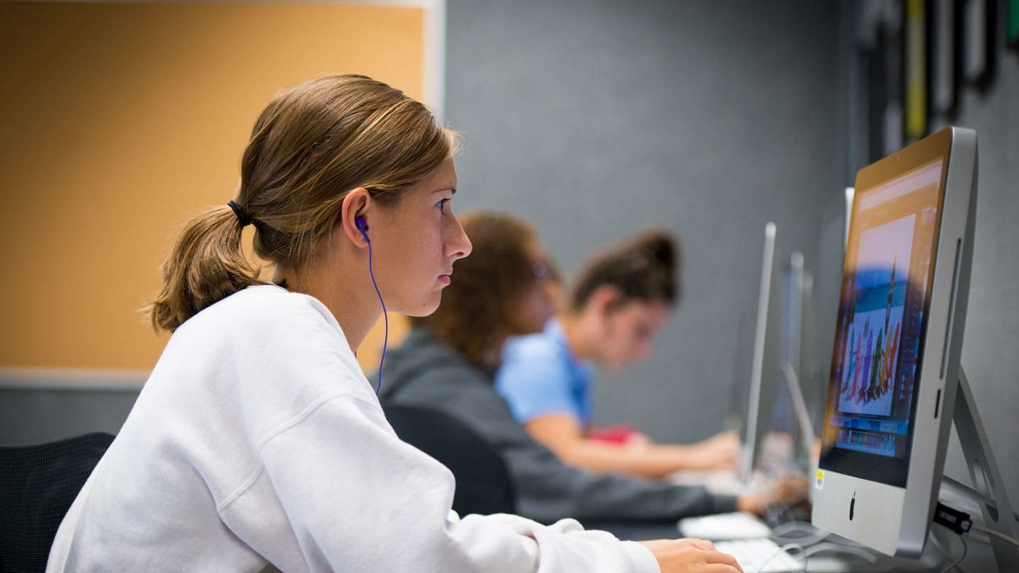 Graphic design student wearing a white sweater works in the design lab