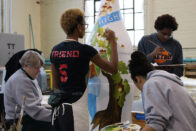 Group of students and alums working with O'Neil to paint bottle sculpture in the studio