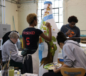 Group of students and alums working with O'Neil to paint bottle sculpture in the studio