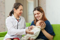 Nurse examining baby sitting on mother's lap