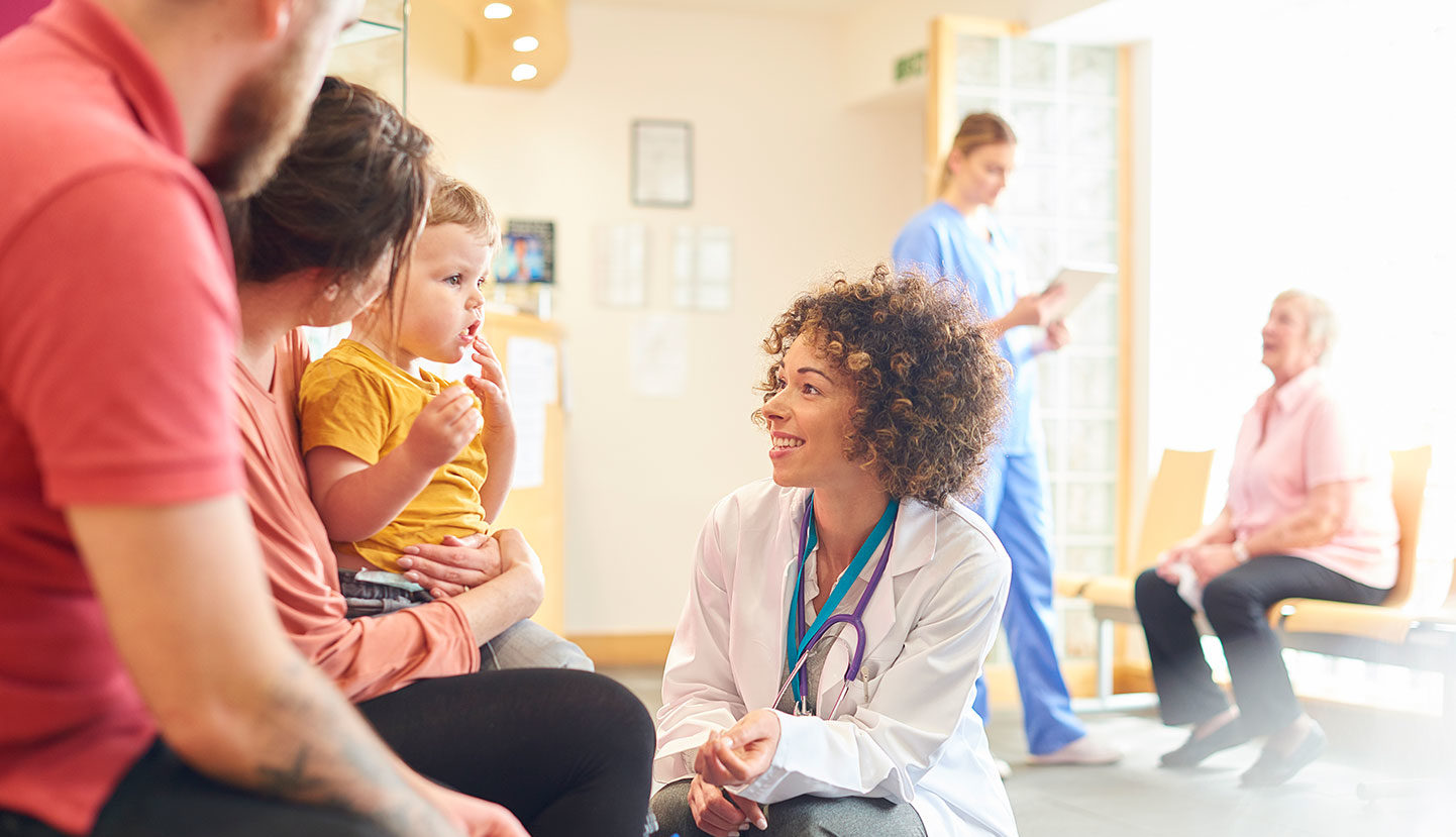 Nurse kneeling in front of parents with baby in clinic