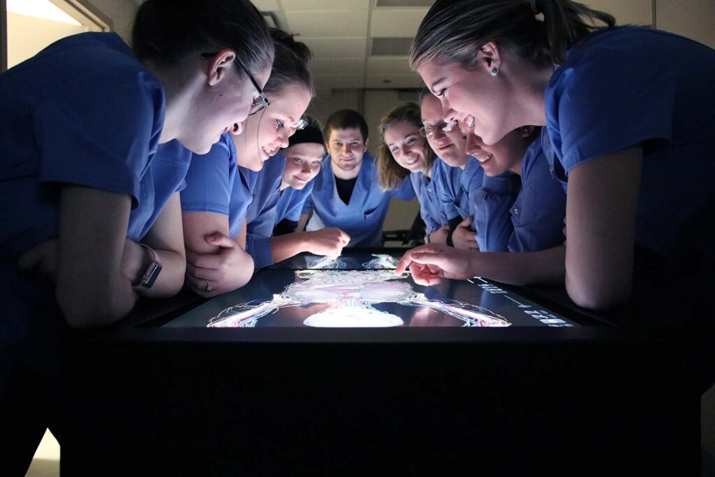 Nursing students crowded around tabletop screen looking at anatomy model