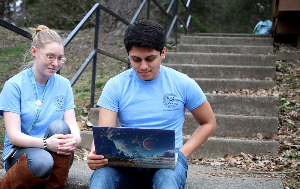 Two Pomeroy Scholars sitting on stairsteps looking at laptop