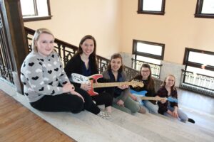 Group of music therapy students sitting on the conservatory stairs holding the custom-built guitars