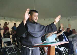 Friar Mario stands with his hands lifted up in a blessing over the lake