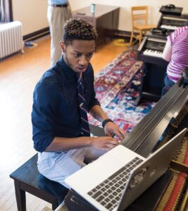 Brewer playing a piano while watching a laptop in a music class.