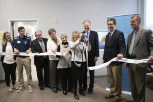 Staff, students and community members hold a ribbon as President King cuts it with a large pair of scissors.