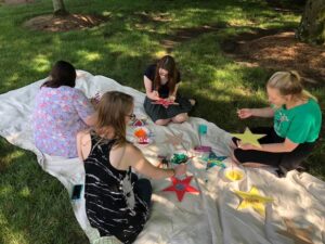 Group of MAMT students sit on a blanket painting stars.