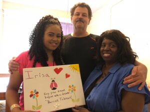 Brown holds up piece of artwork with her parents standing in her new dorm room