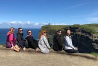 Group of SMWC choir students sitting facing the Cliffs of Moher