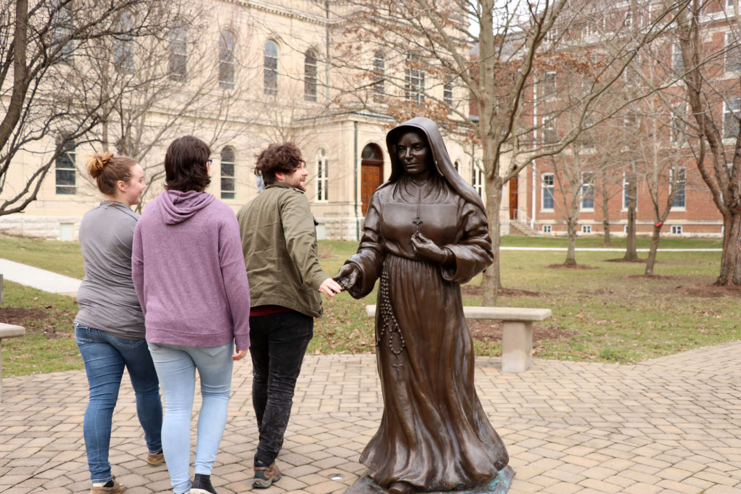 Students touch the hand of Saint Mother Theodore Guerin as they walk past the statue.