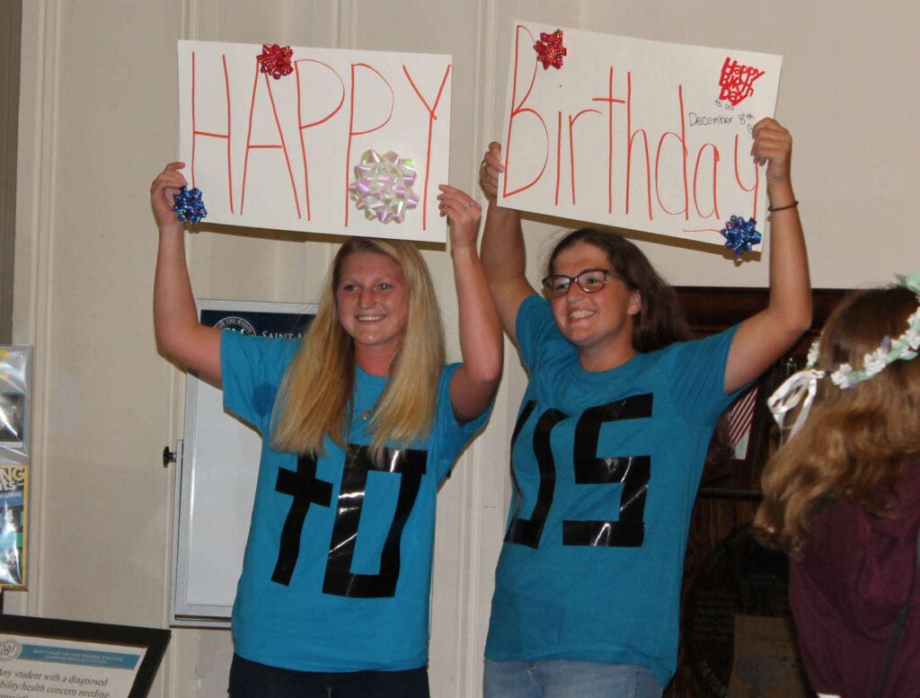 A big and little with signs and shirts that read together "happy birthday to us"