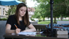 Student sits at a table outside making notes on a paper.