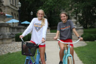 Smiling students sitting on bikes in front of Guerin Hall