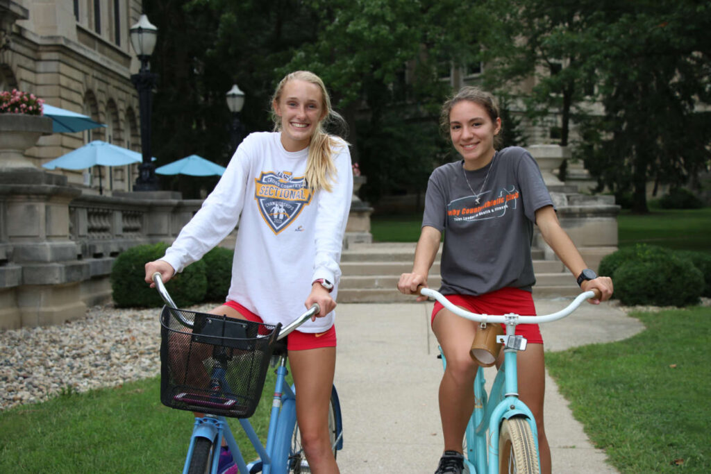 Two students sitting on bikes at the path in front of Guerin Hall