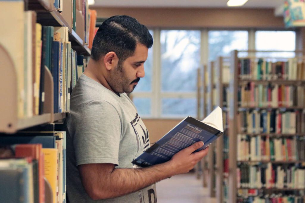 Student reading book standing in the library stacks