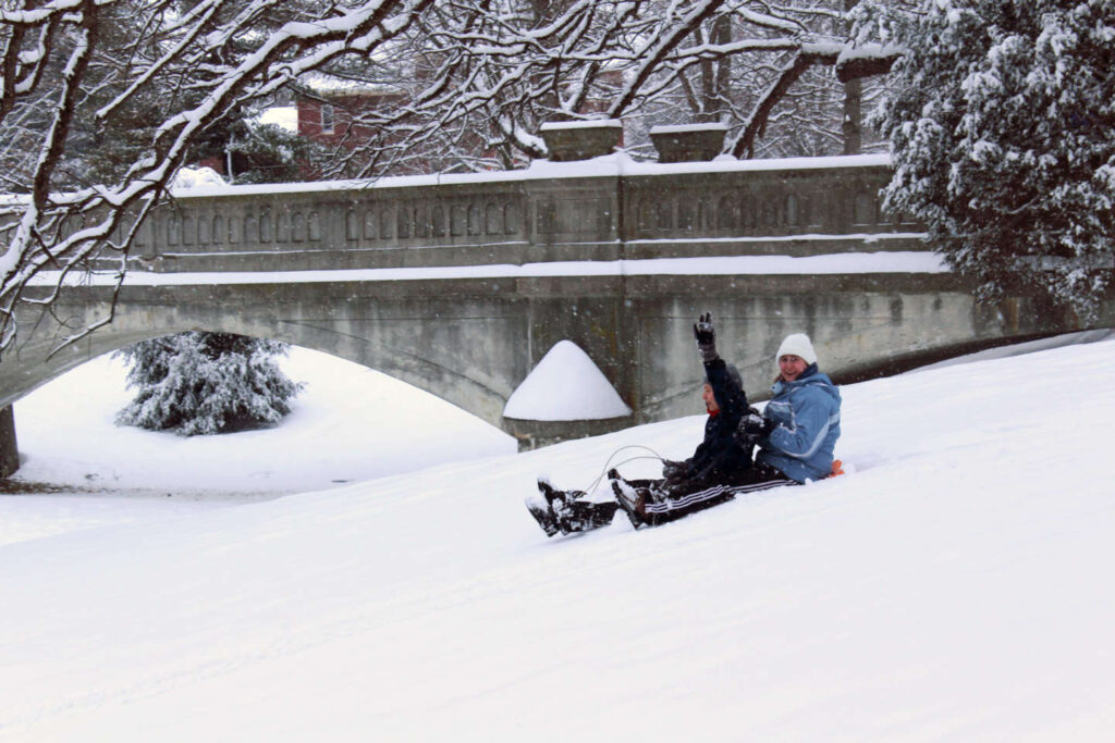 Students fly down the sledding hill with the Grotto Bridge in the background