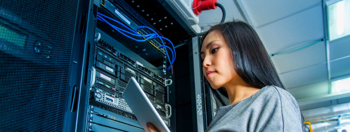 Woman holding tablet standing next to a server rack.