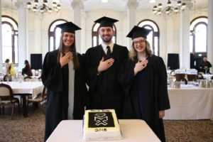 three students celebrate Ring Day around a cake