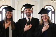 three students celebrate Ring Day around a cake
