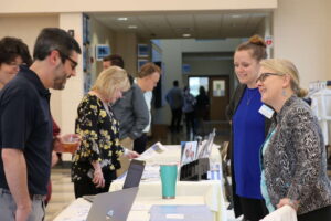 Faculty standing at tables in the atrium talking with staff