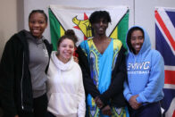 Students stand for a group photo in front of flags at an International Week event