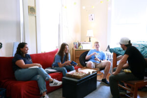 Four students eating pizza and chatting in a dorm room