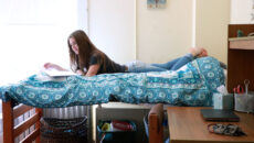 A student laying on a bed studying in a dorm room