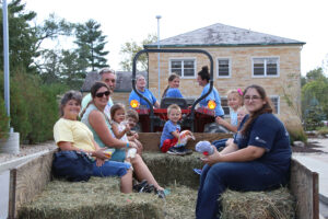 Group of alumni riding on tractor and hay-filled trailer