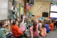 Class of elementary students raising hands to answer a question