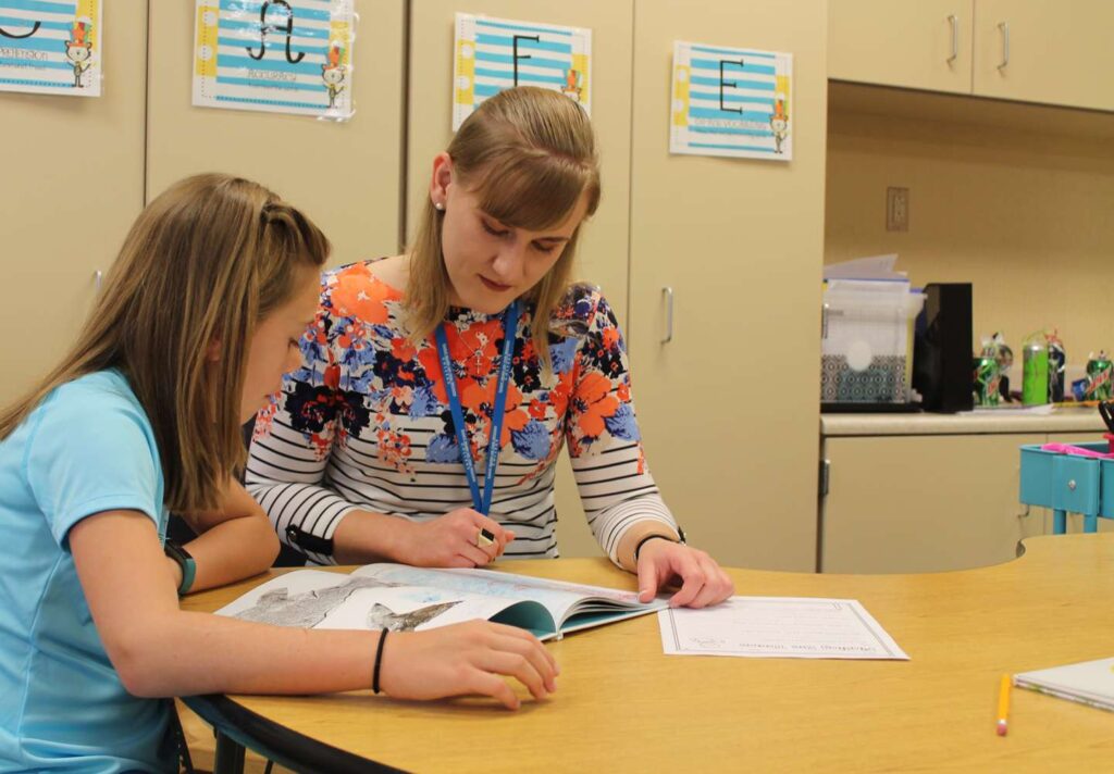 A teacher helps a young student learn to read.