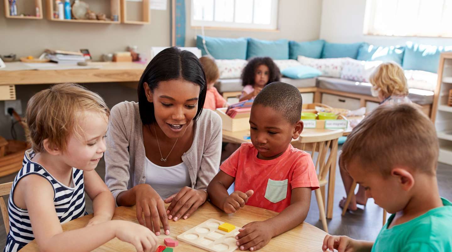 Teacher helping children learn to put blocks into a puzzle.