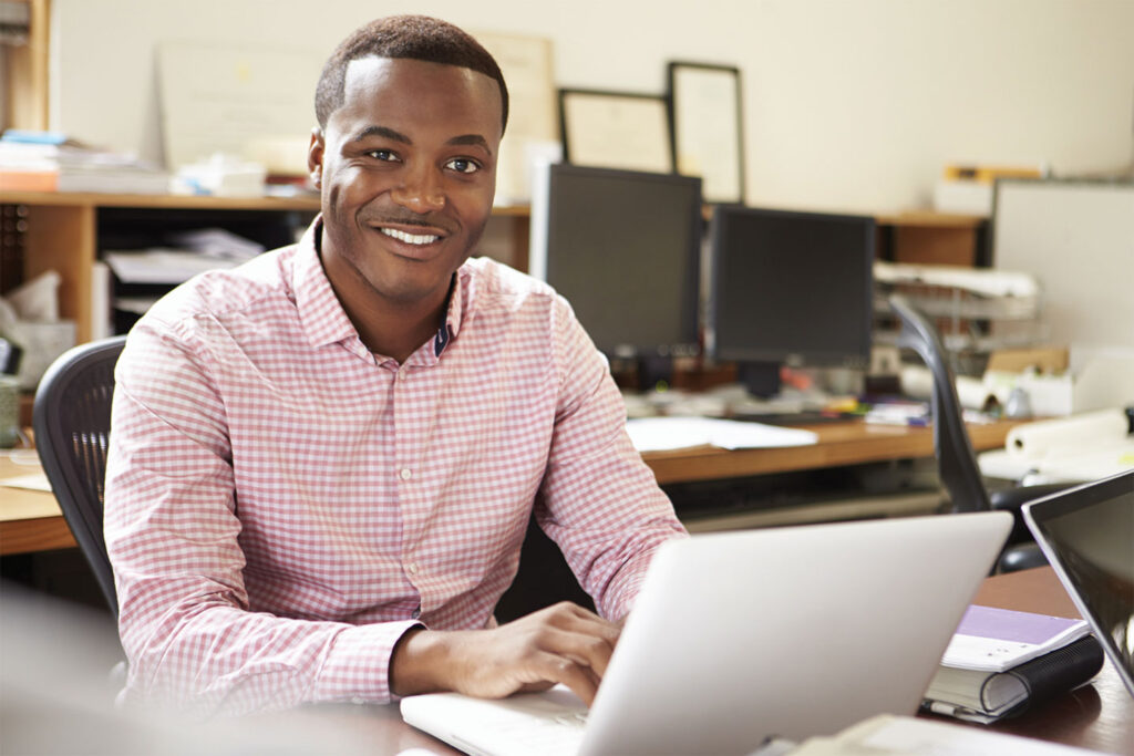 Younger man looking up from laptop at desk