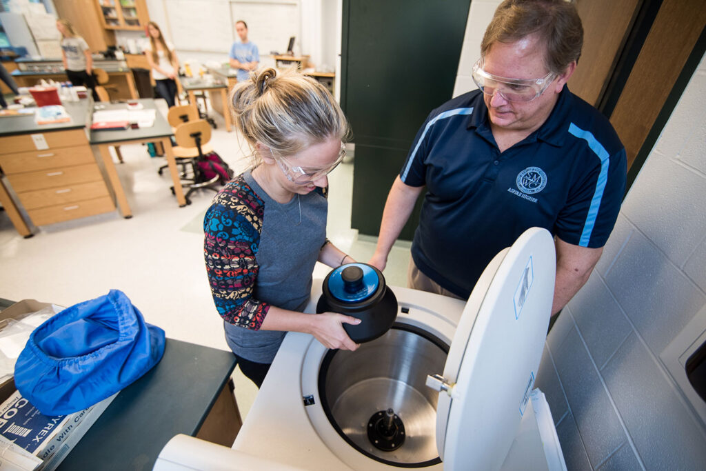 Professor helping student place sample in centrifuge