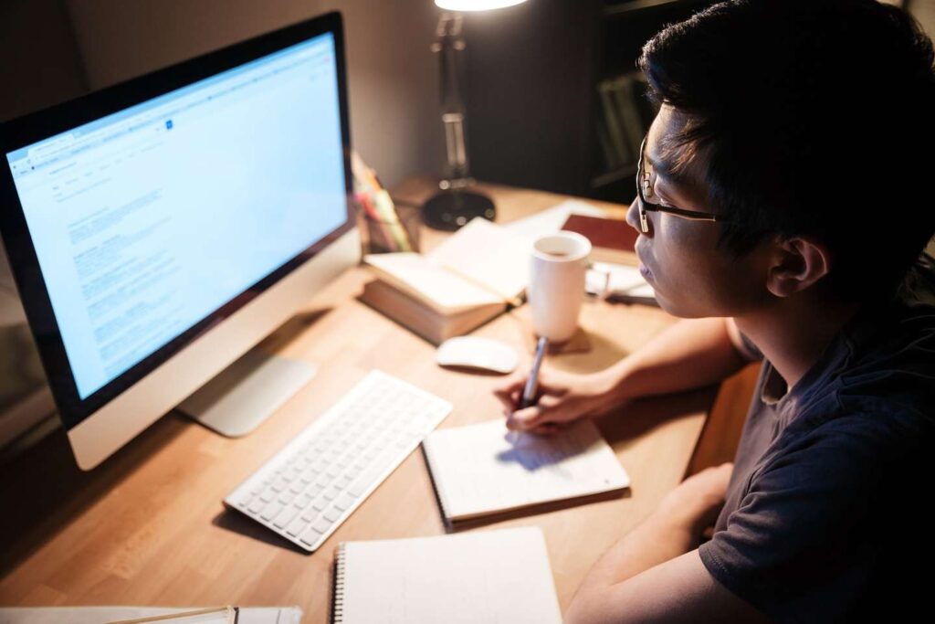 A male student studying in the evening light at his desk.