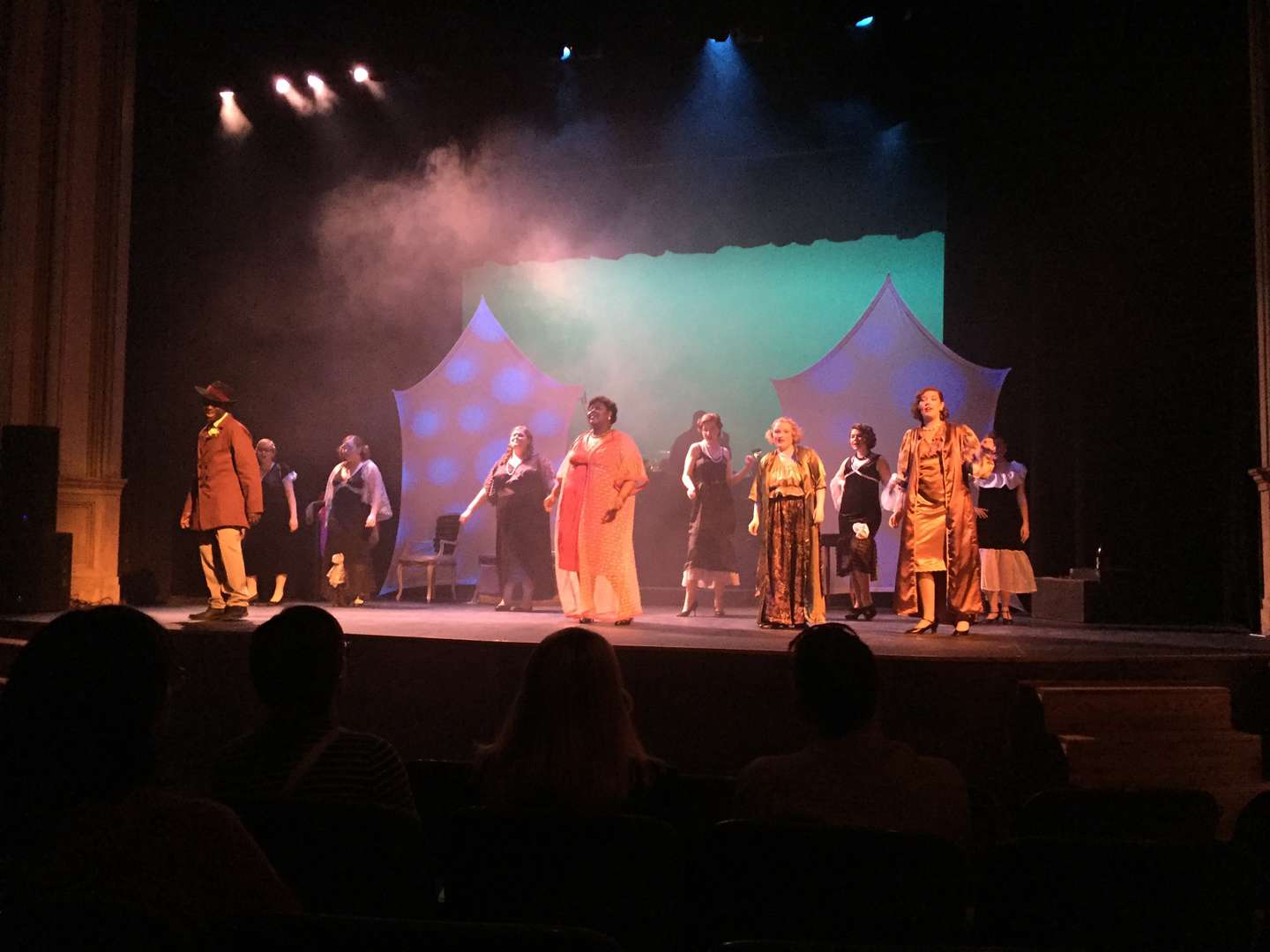 Bright lights shine and a little smoke shows, as a full cast of students in costume dance and sing on a stage.