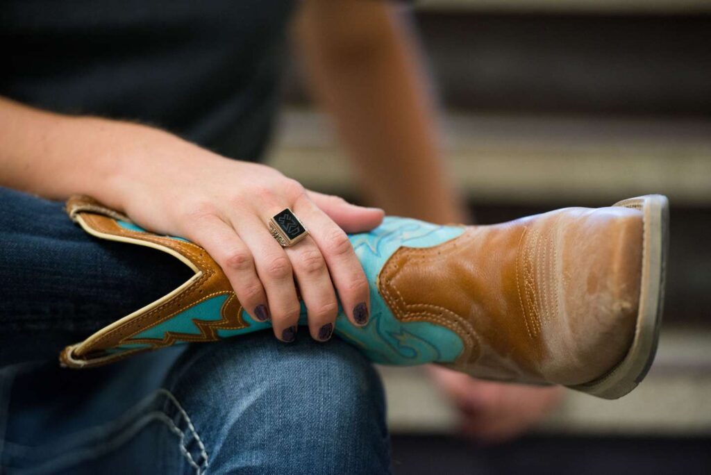 A close-up of an equine student's cowboy boot with her hand and Woods Ring holding onto it.