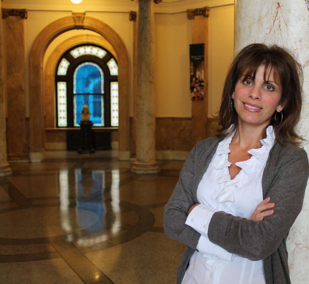 Christy Ellis leans on one of the marble columns in the Rotunda smiling.