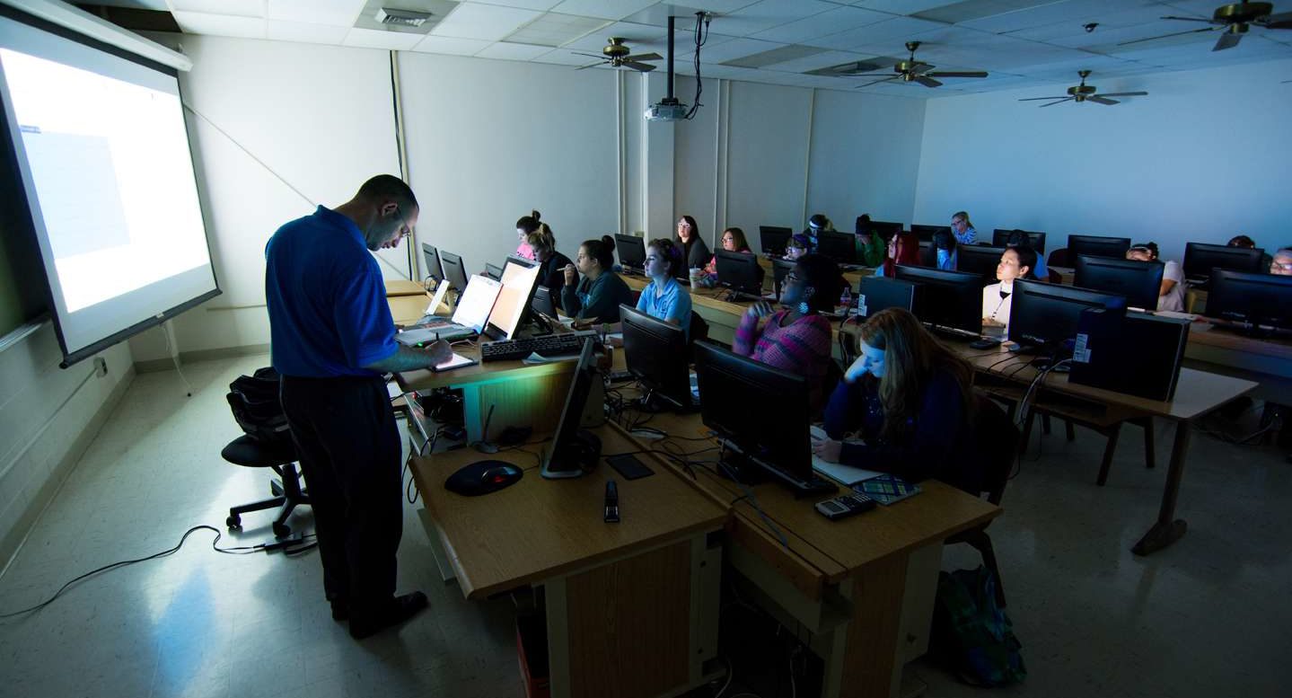 A computer classroom with low light as an instructor teaches.