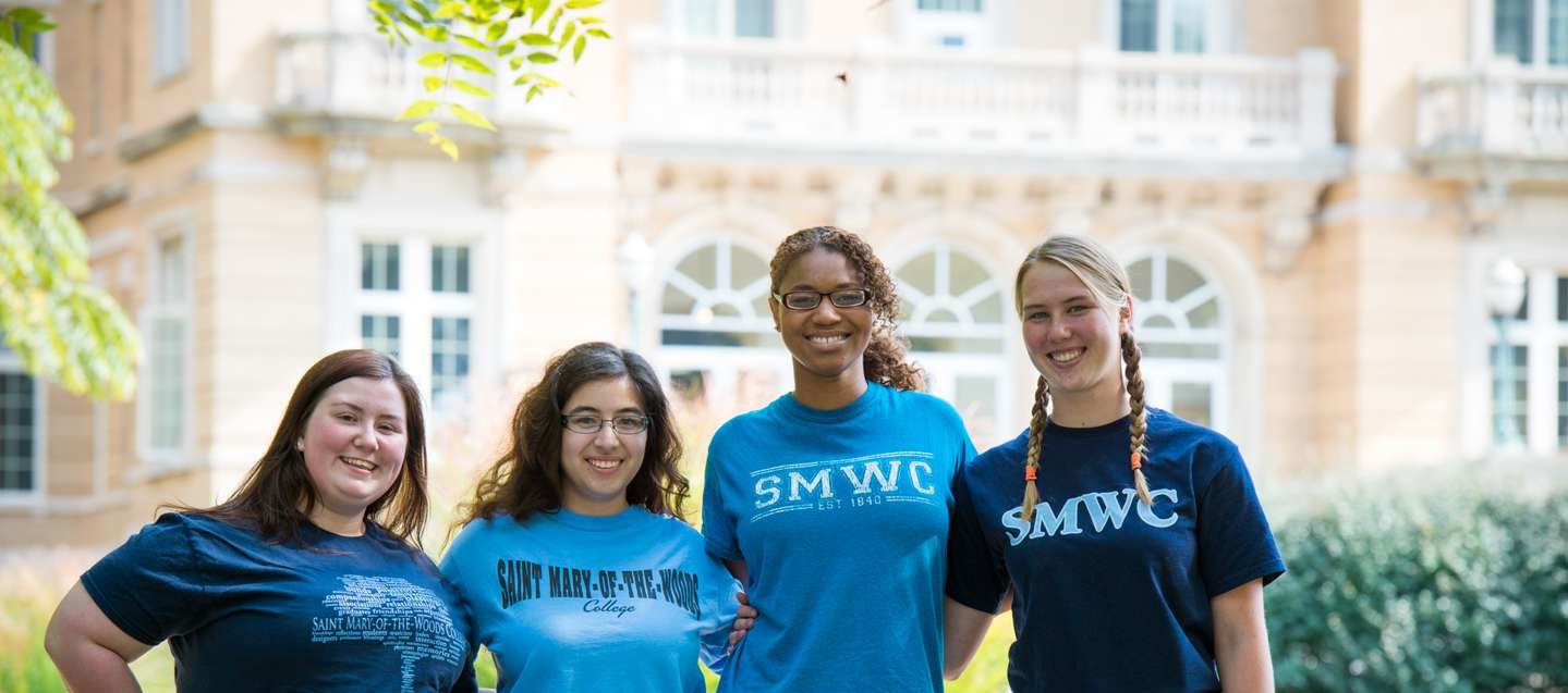 Four female student with arms linked and SMWC t-shirts smiling.
