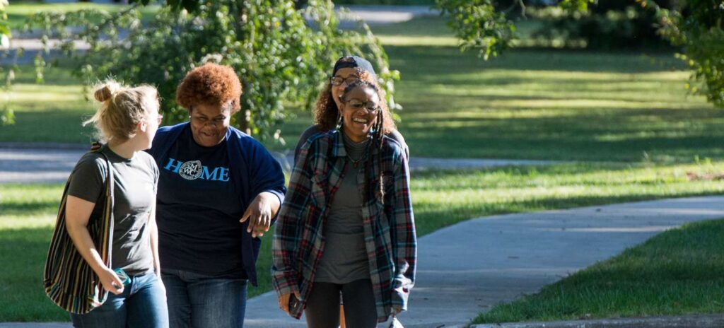 Four women walking together on campus laughingh and smilinng.