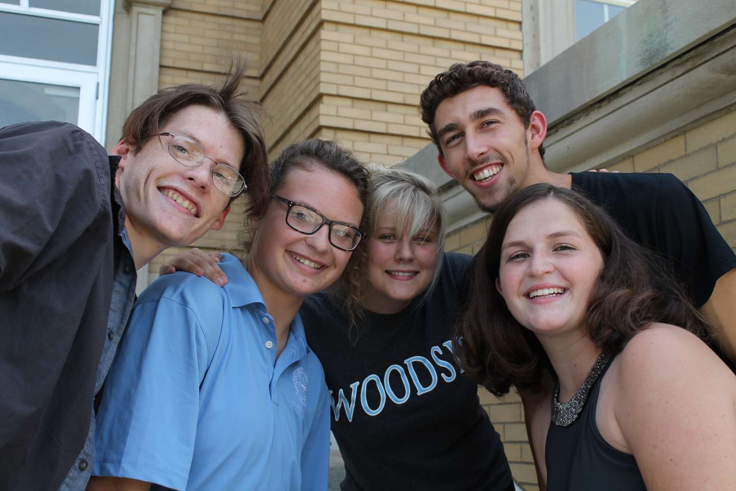 Two males and three females with their heads together smiling.