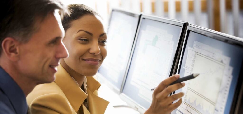 A man and woman at a computer, as the woman is pointing to a graph on the screen.