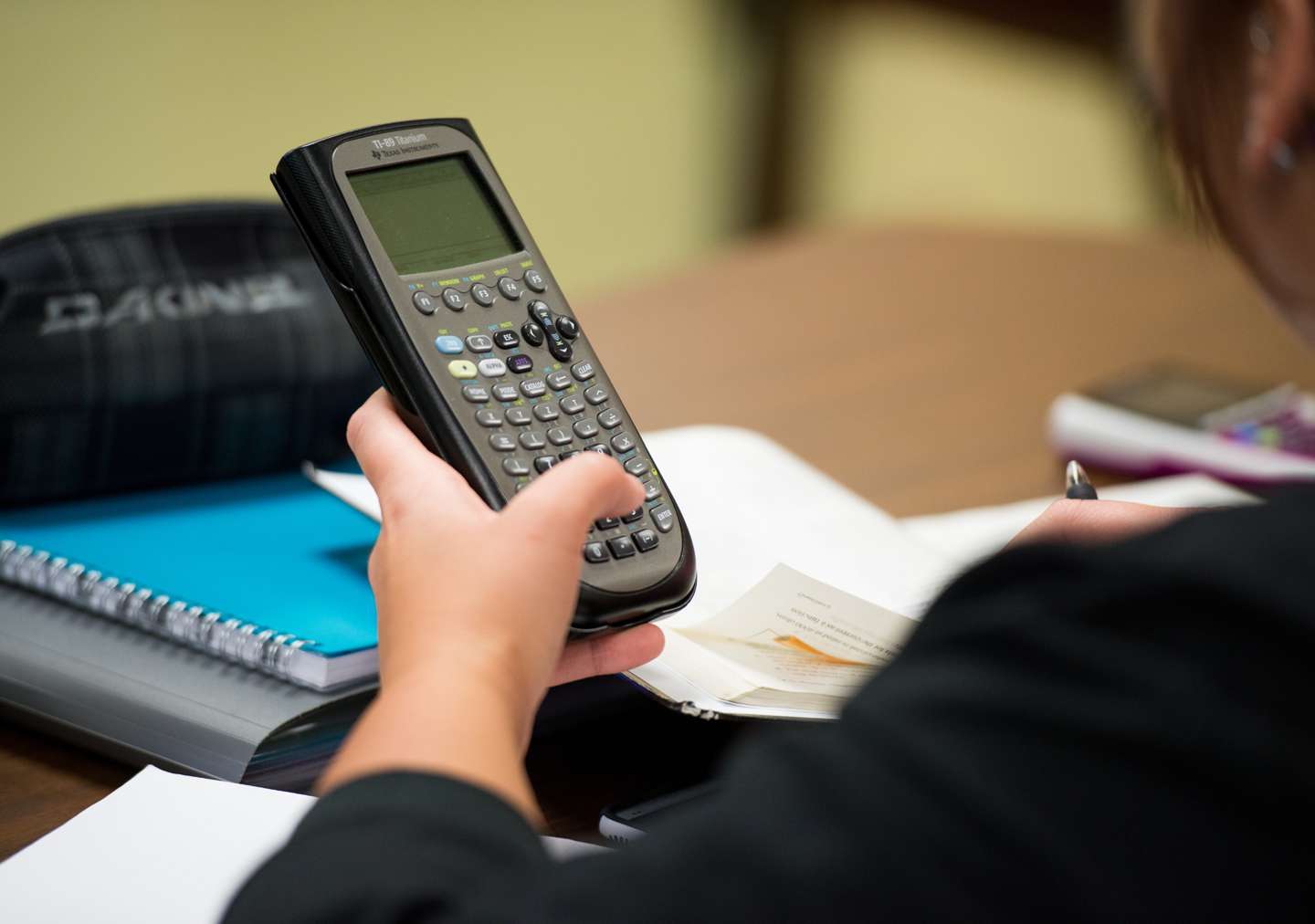 The hand of a student holding a graphing calculator and working on an assignment.