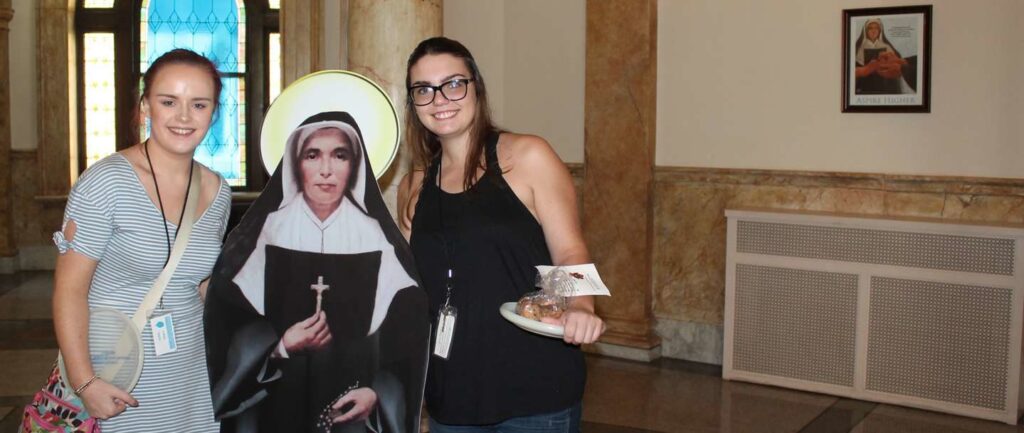 Two female student on each side of Flat Saint Mother Theodore Guerin smiling.